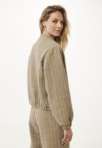 Teksturowana, oversize beżowa kurtka z żebrowanym dołem i mankietami, z delikatnym wzorem i luźnym krojem. Noszona na dopasowanych spodniach.