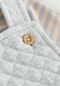 Grau gestepptes Gewebe mit einem Knopfdetails, das ein vierblättriges Design zeigt. Der Hintergrund besteht aus beige und grau gestreiftem Stoff.