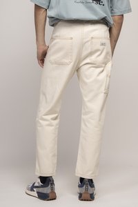 Pantalons beige clair à coupe décontractée, avec deux poches au dos et une poche sur le côté, associés à des baskets bleu marine et grises.