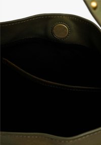 Interior de bolso de cuero verde oliva con forro de tela negra, que cuenta con un cierre a presión de metal y bordes cosidos para mayor durabilidad.