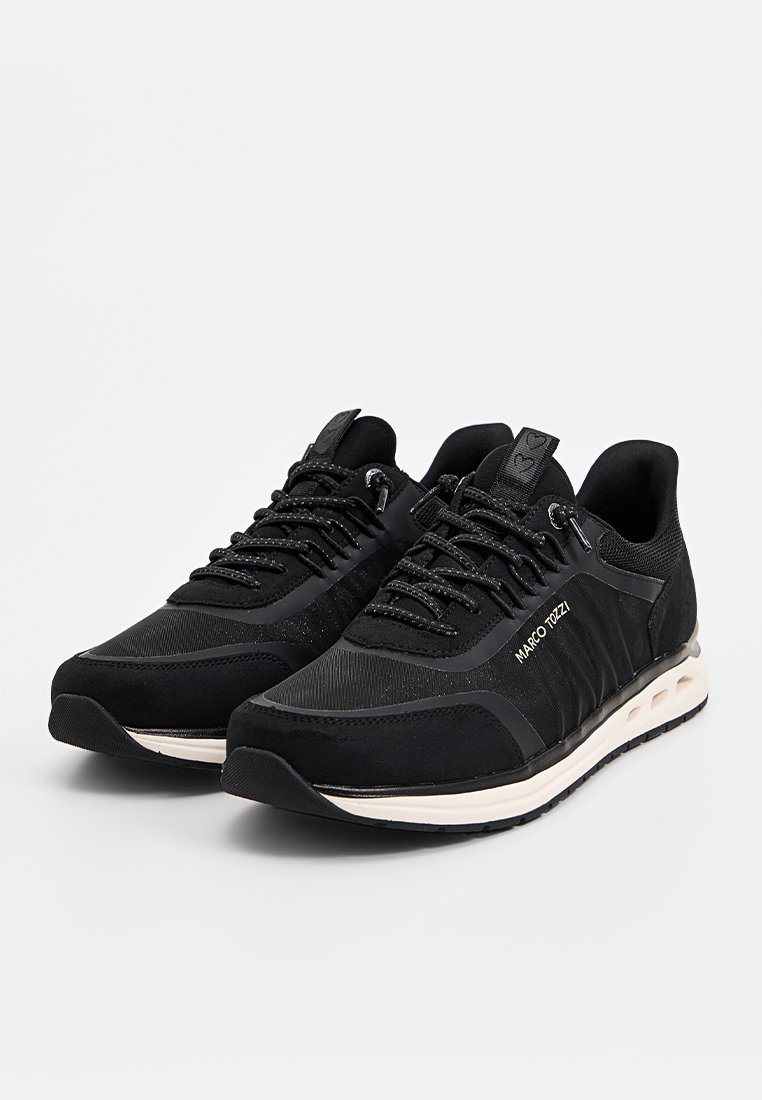 Chaussures de sport noires en mesh et suède, avec un design texturé, des lacets plats et une semelle intermédiaire blanche avec des découpes circulaires.