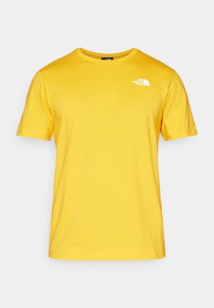 Žluté bavlněné tričko s krátkým rukávem, kulatým výstřihem a bílým logem na levé hrudi. Tkanina vypadá hladce a lehce.