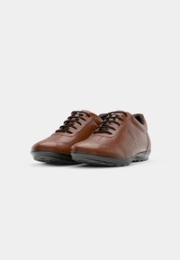 Brown leather shoes with a smooth texture, featuring black laces, a rounded toe, and a flexible rubber sole. Minimal design with subtle stitching.