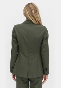 Olivgrüner taillierter Blazer mit einer figurbetonten Silhouette, strukturierten Schultern und Ein-Knopf-Manschetten. Hergestellt aus glattem Stoff mit einer dezenten Textur.