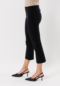 Pantaloni neri a culotte realizzati in tessuto elastico, caratterizzati da una vita aderente, bordo svasato e una texture liscia abbinati a tacchi a punta neri.