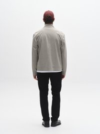 Grå jacka med texturerad yta, svarta byxor och svarta skor. Bakifrån syns en vinröd mössa, krage och avslappnad siluett.