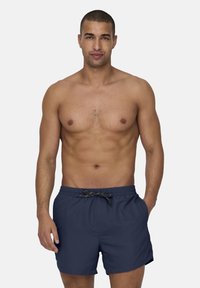 Bañadores de hombre en color azul marino, confeccionados en una tela ligera y de secado rápido. Cintura elástica con cordón, cuenta con bolsillos laterales y un corte recto.