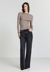 Gestreiftes, beiges Langarmoberteil, kombiniert mit hoch taillierten, weiten schwarzen Jeans. Der Stoff hat eine weiche Textur und die Jeans verfügen über normale Taschen.