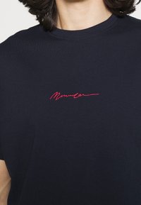 Mörkblå bomullströja med korta ärmar och rundad hals, prydd med röd broderad text på bröstet.