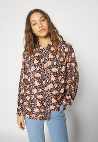 Blusa floral en negro con flores rosas y naranjas; presenta cierre de botones, mangas largas y un corte relajado. Tela suave con una textura lisa.