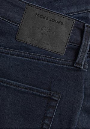 Dunkelblaue Denim-Jeans mit einem schwarzen rechteckigen Lederetikett, auf dem "Jack & Jones Jeans Intelligence Since 1990." steht.