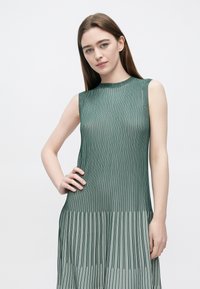 Vestido verde sem mangas com riscas verticais, tecido de malha texturada, decote redondo e silhueta fluida.