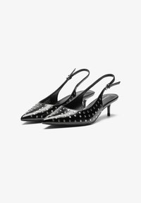Tacchi a slingback neri con punte affusolate, dettagli borchiati e tacco sottile. Realizzati in materiale lucido con una texture liscia.