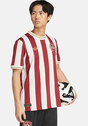 Maillot de football rayé rouge et blanc avec un col rond côtelé, des manches courtes et un logo brodé. Porté avec un short noir et un ballon de football.