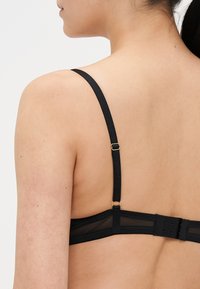 Reggiseno nero con spalline lisce, dettagli in rete e fibbie regolabili. Presenta una chiusura posteriore con più ganci per una vestibilità sicura. Design semplice.