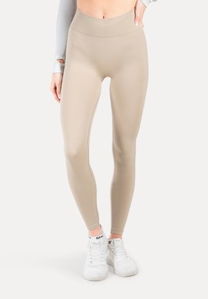Leggings de talle alto en color beige, hechos de una tela elástica, con una textura suave y un diseño ajustado. Combinados con zapatillas deportivas blancas.