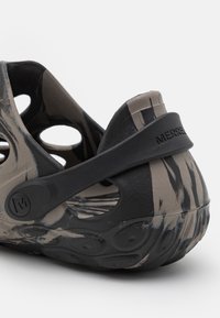 Gros plan sur un sabot Merrell marbré noir et beige avec des trous de ventilation et une sangle au talon ajustable.