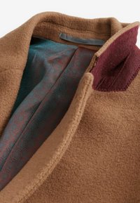 Bruine wollen jas met een pluche textuur, voorzien van een teal binnenvoering met een subtiel hexagonaal patroon, en een bordeauxrode kraagaccent.