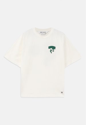 T-shirt en coton couleur crème à manches courtes, avec un design graphique vert sur la poitrine et une petite étiquette logo en bas.