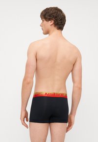 Boxeri negri, cu talie cu logo-ul Nike roșu și auriu. Material neted, design mulat, lungime până la mijlocul coapsei, fără modele sau accente vizibile.