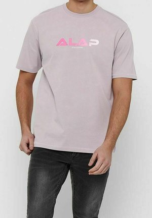 Camiseta corta de manga corta color púrpura claro, hecha de algodón, con un atrevido estampado gráfico en texto rosa en la parte frontal. Combinada con jeans oscuros.