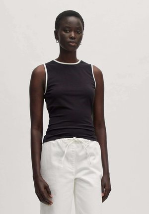 Schwarzes ärmelloses Top mit weißem Kragenbesatz, figurbetontes Design, kombiniert mit wei�ßen Stoffhosen mit Kordelzug, die eine glatte Stoffoberfläche zeigen.