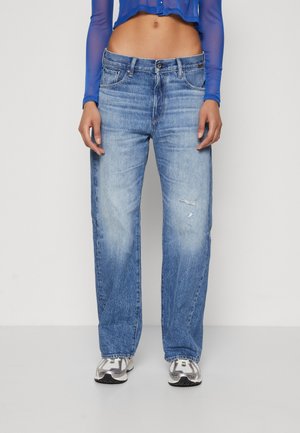 Person iført lyseblå vaskede straight-leg jeans med mindre slid, hvide og grå sneakers og en let blå langærmet cropped top.