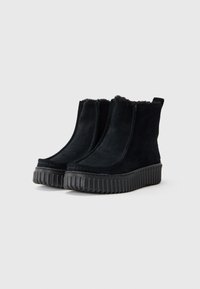 Bottines en suede noir avec une semelle en caoutchouc rainurée, dotées d'un doublure intérieure douce et de détails de couture minimalistes le long des bords.