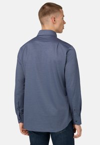 Ilgas rankovės marškiniai tamsiai mėlynos spalvos, su plačiu apykakle, mygtukų rankogaliais ir lygiu tekstūru. Nugarinė dalis turi paprastą, tvarkingą dizainą.