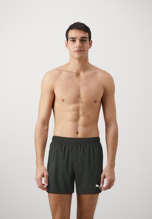 Shorts de bain vert foncé avec taille élastique, poches latérales et un logo blanc sur la partie inférieure de la jambe gauche. Tissu lisse et léger.