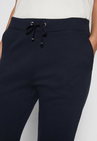 Pantalones de chándal azul marino hechos de tela suave, con cintura ajustable, bolsillos laterales y una textura lisa con detalles de costura mínimos.