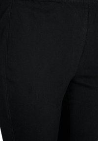 Tejido de mezclilla negra, de forma ajustada, que presenta una textura sutil con un acabado suave. Los detalles incluyen costuras a lo largo de las costuras.