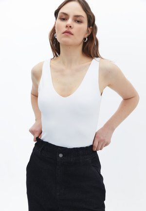 Body blanc ajusté avec un décolleté en V profond et de larges bretelles, associé à un pantalon en denim noir taille haute avec une ceinture élastique.