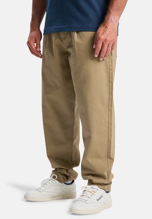 Beige loose-fitting cotton pants with front pleats, paired with white sneakers featuring blue accents. Simple design, no visible patterns.