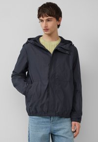 Marineblauwe lichtgewicht jas met een capuchon, elastische manchetten, twee voorzakken en een ritssluiting. Gemaakt van een gladde, waterafstotende stof.