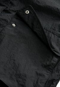 Tessuto nero con texture e gocce d'acqua. Presenta una tasca frontale e chiusure a scatto in metallo. Finitura opaca generale con una leggera lucentezza.