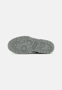 Suela de zapatilla Puma gris con patrones de tracción circulares y lineales, que presenta el logo de Puma y el texto "Diseñado por Puma".