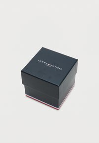Square, dark blue cardboard box with a lid; features a white logo reading "TOMMY HILFIGER" and a tri-color stripe on the base.