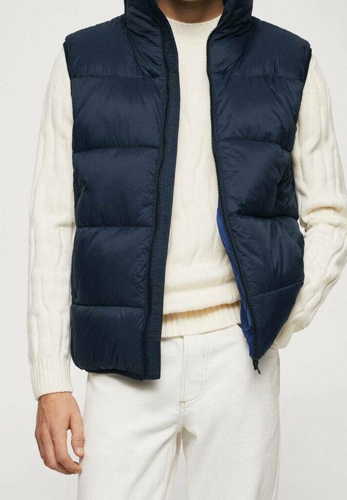 Laivaston sininen puhviliivi, jossa on korkea kaulus ja etuvetoketju. Varustettu vaakasuorilla tikatuilla paneeleilla ja sileällä, kiiltävällä pinnalla. Yksityiskohtana kermaharmaa neule.