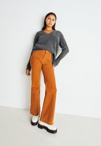 Gray v-neck sweater over orange corduroy flared pants. The model wears white chunky platform boots with a thick black sole.