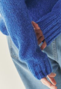 Niebieski dziany sweter o strukturalnym wykończeniu, z długimi rękawami i ściągaczami, w zestawie z jasnymi dżinsami.