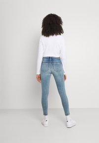 Tunna blå jeans i denim med blekning, med medelhögt midjeband, två bakfickor och i kombination med vita sneakers.