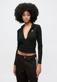 Μαύρο κοντό μπουφάν με φερμουάρ, ριμπ υφή και ψηλό γιακά, με μικρό λευκό λογότυπο Adidas στο αριστερό στήθος.