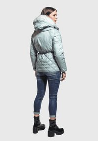 Chaqueta acolchada de color azul claro con capucha, cintura ceñida y puños elásticos, combinada con jeans de mezclilla oscura y botas de plataforma negras.