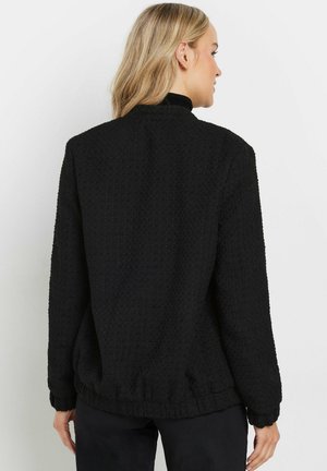 Veste noire texturée avec un col haut, des poignets côtelés et un ourlet. Présente un motif gaufré subtil et une coupe décontractée. Vue arrière présentée.
