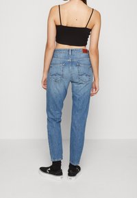 Jeans de mezclilla azul claro con cintura alta, pierna ajustada y dos bolsillos traseros. Combinados con zapatos negros de tipo slip-on y calcetines negros hasta el tobillo.