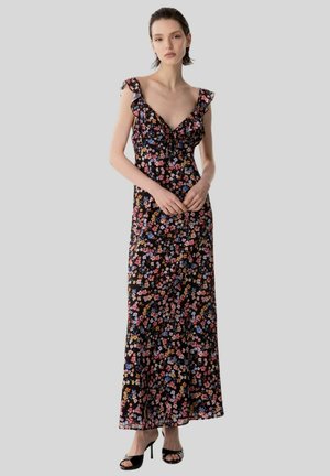 Donna che indossa un abito lungo nero senza maniche con stampa floreale multicolore e spalline arricciate, abbinato a tacchi neri open-toe.