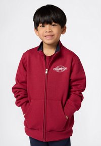 Bordeaux kleurige zip-up sweatshirt van zachte stof, met een marineblauwe kraag, zijzakken en een witte "Champion" logo op de borst.
