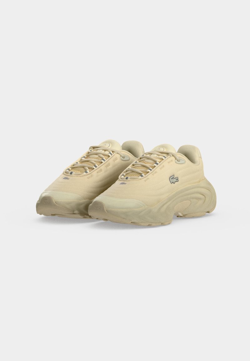Coppia di sneakers beige con lacci, suole spesse curve e un piccolo logo a coccodrillo sul lato, mostrati su sfondo bianco.