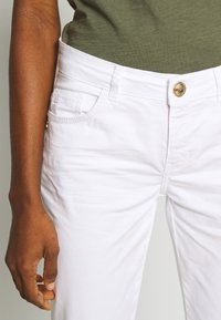 Vita bomullstrosor med slim fit, med framfickor, knappstängning och subtila sömnadsdetaljer längs sömmarna.